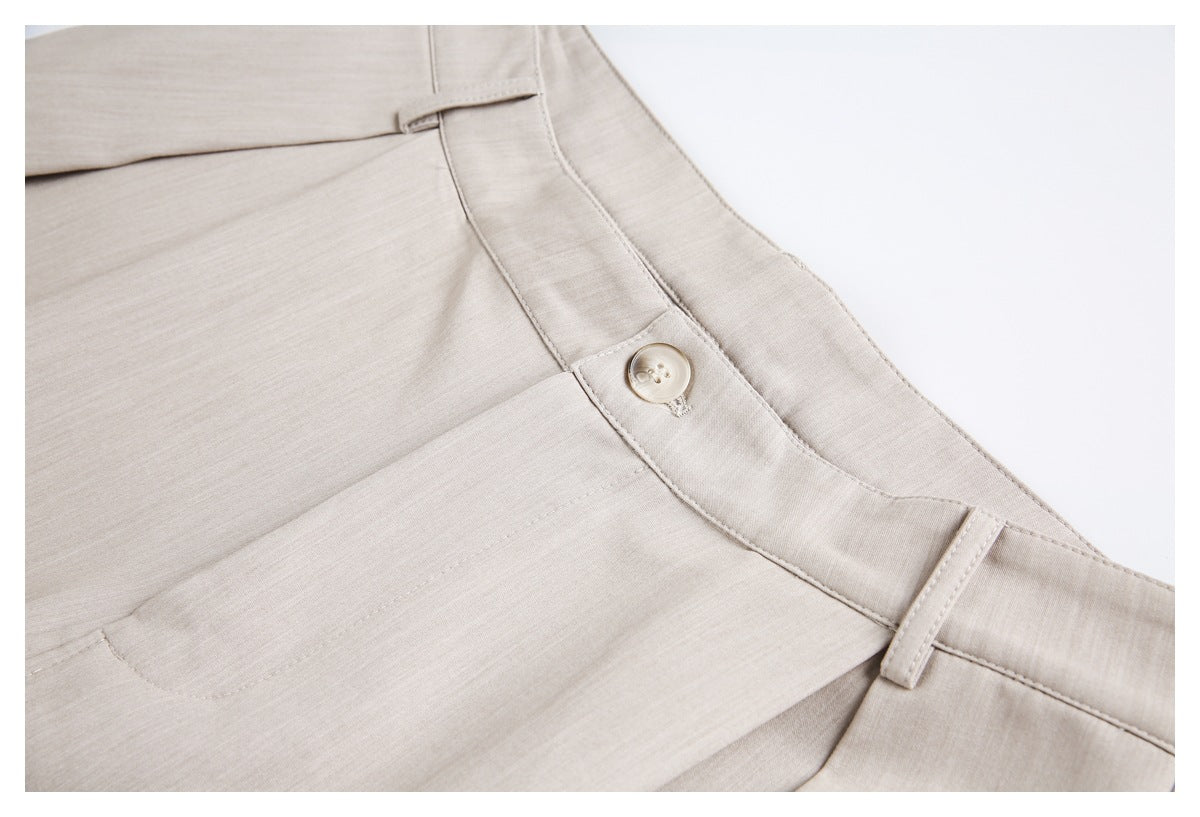 Close-up of beige trousers showing the front button, waistband, belt loop, and pocket opening.