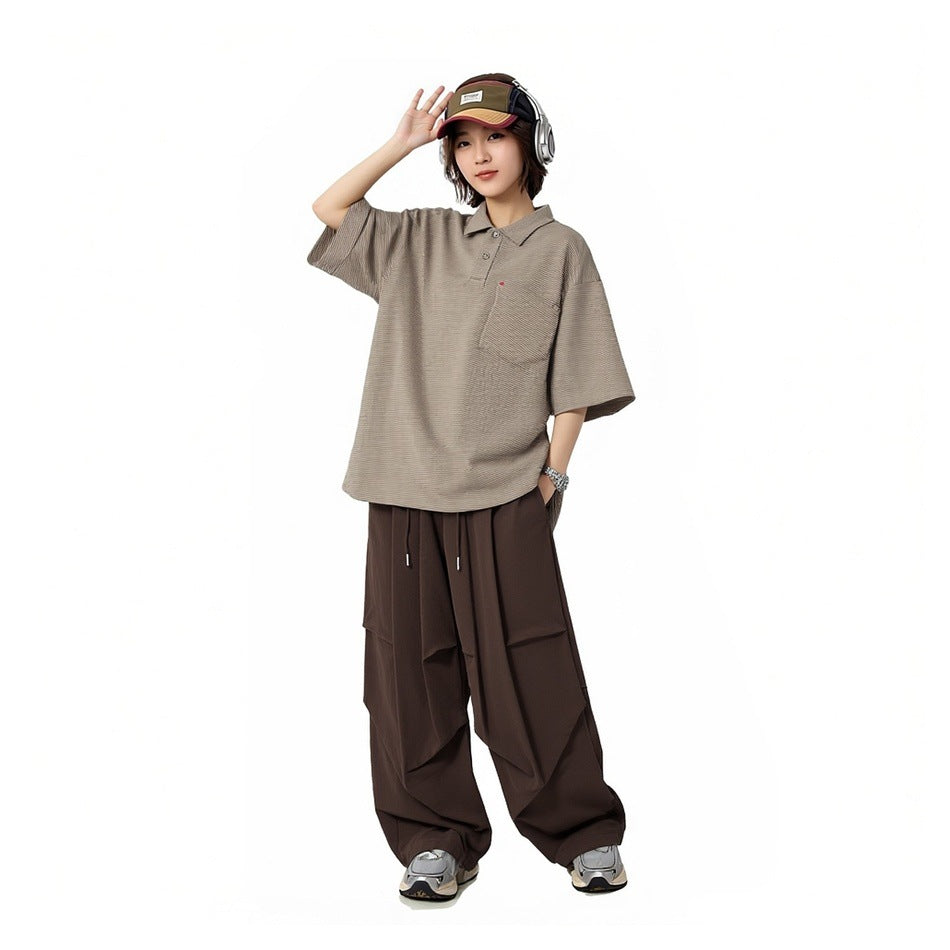 Model wearing khaki-green striped polo shirt with brown wide-leg pants, cap and headphones