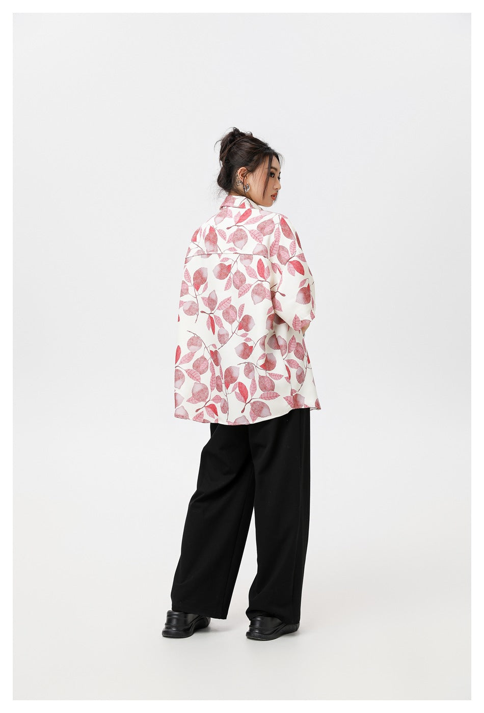 Back view of a model wearing an oversized pink leaf-print short-sleeve shirt with black wide-leg pants