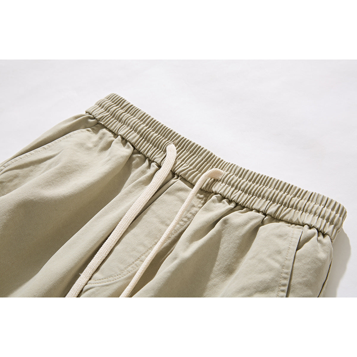 Close-up of beige trousers showing an elastic waistband, white drawstrings, and a front pocket.