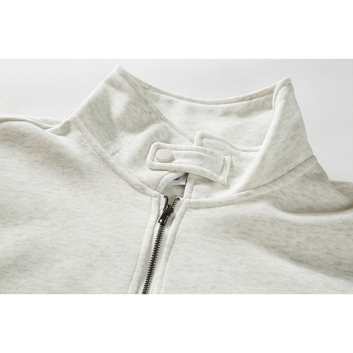 Close-up of an off-white quarter-zip sweatshirt collar with a snap-tab closure and metal zipper.