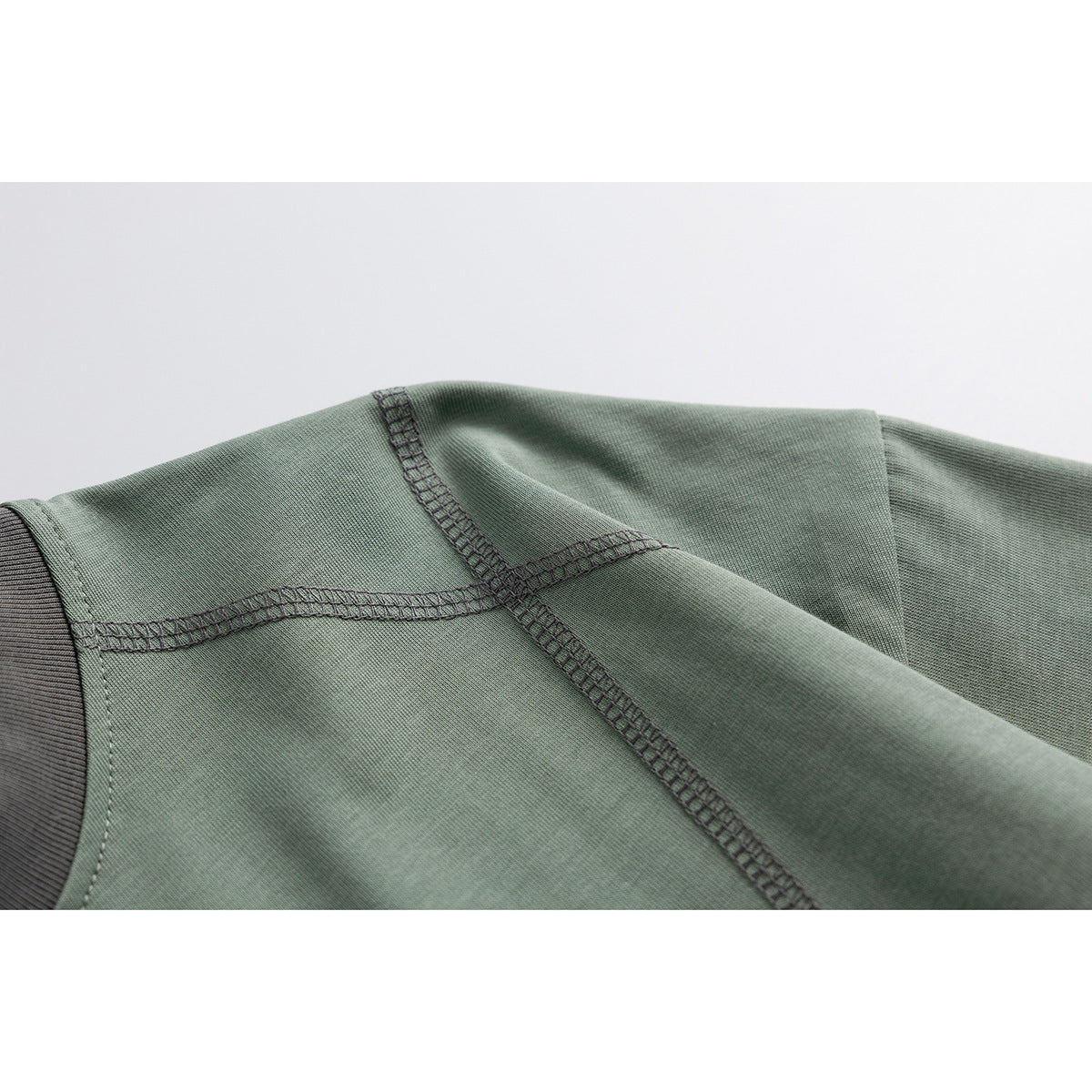Close-up of the sage green T-shirt's shoulder and sleeve seams, with dark contrast stitching.