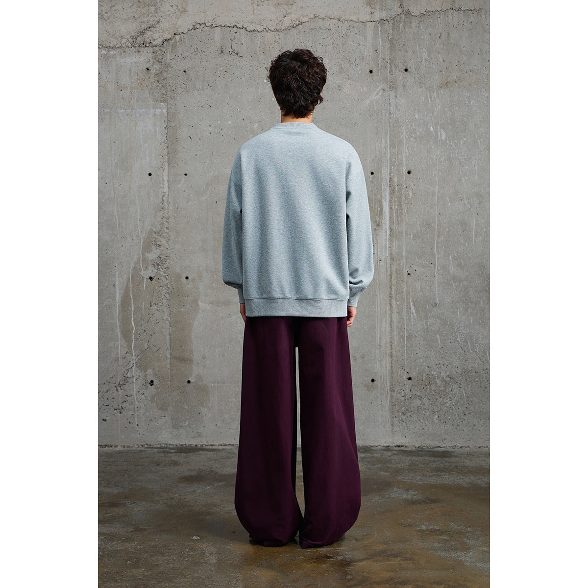 Back view of a model wearing a light gray crewneck sweatshirt and dark plum wide-leg trousers.