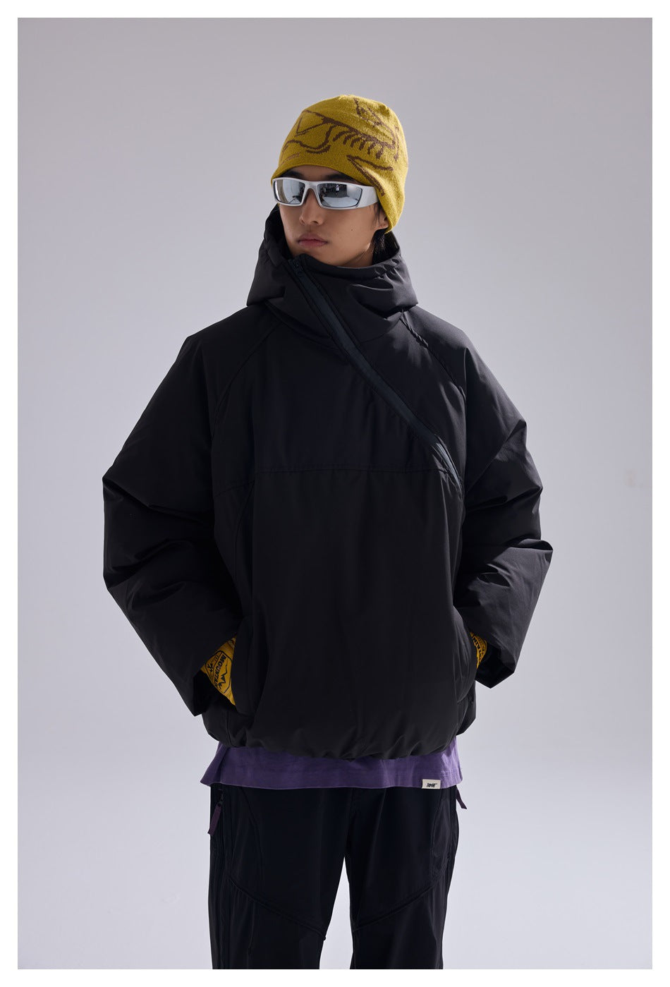 Closer view of a model wearing a black hooded pullover with an angled front zipper and a purple layer underneath.