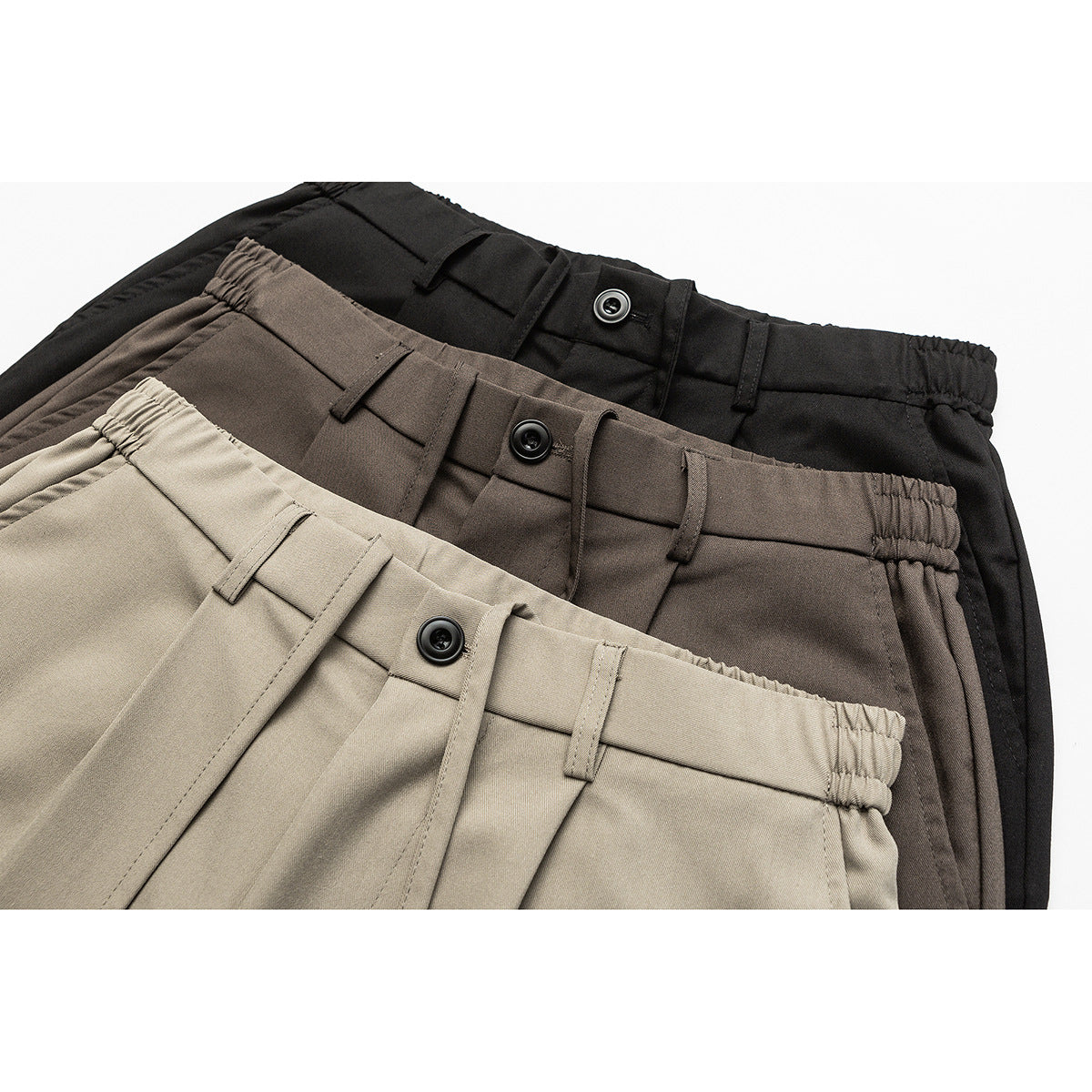 Close-up of three pairs of trousers in black, dark brown, and taupe, showing buttoned waistbands and belt loops.