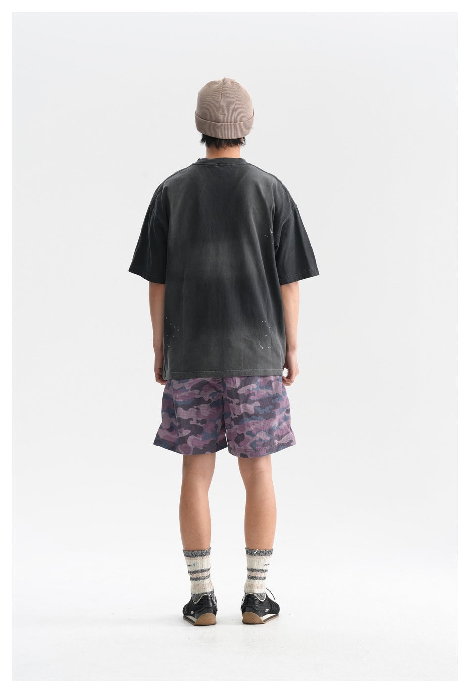 Back view of a person wearing a faded black oversized T-shirt with camouflage shorts and a beanie