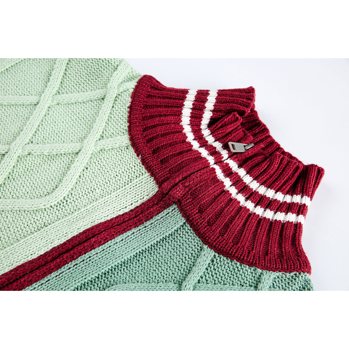 Close-up of a mint-green cable-knit sweater with a burgundy ribbed collar, two white stripes, and a small metal accent.
