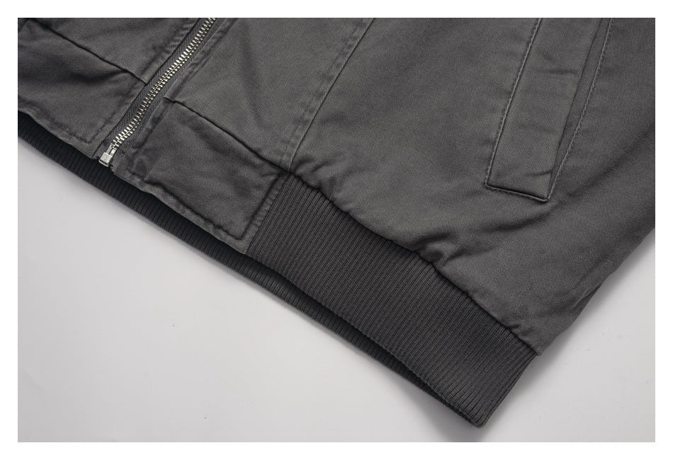 Close-up of a charcoal jacket's ribbed hem, front zipper, and welt pocket.