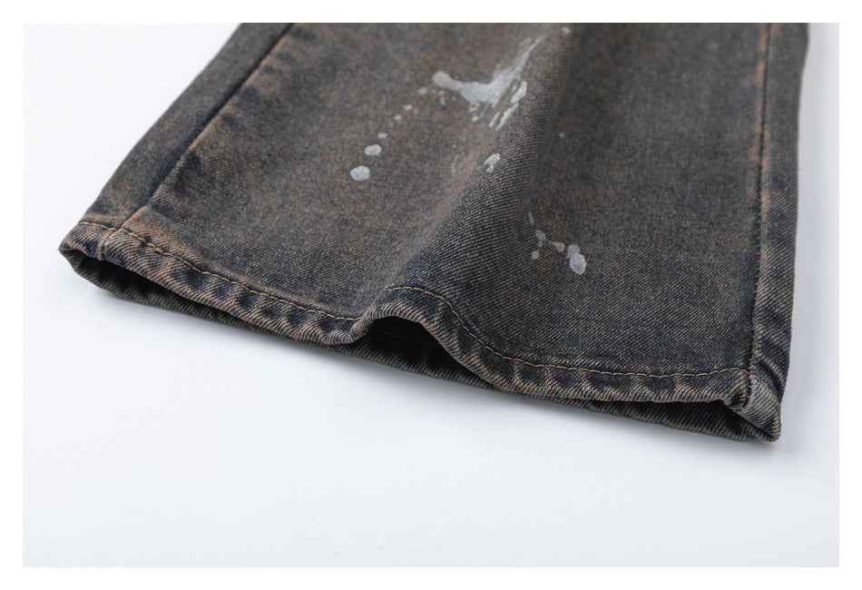 Close-up of a denim trouser leg hem with pale paint-splatter marks.