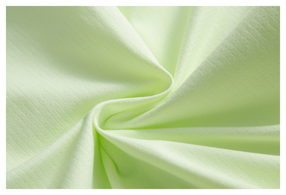 Close-up of pale lime-green fabric draped into soft folds, showing a subtle fine texture.