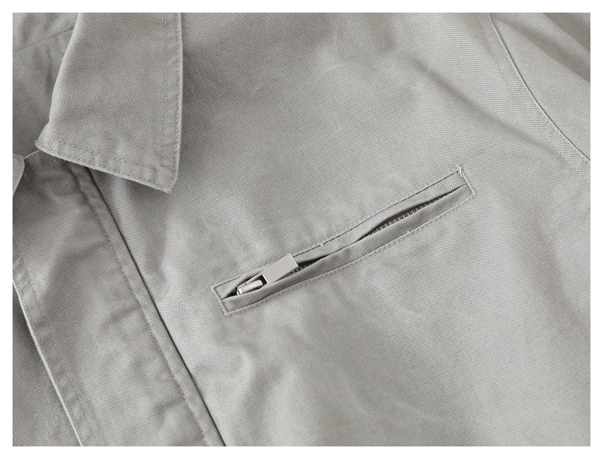 Close-up of a light gray jacket with a narrow diagonal zip pocket and a notched lapel.
