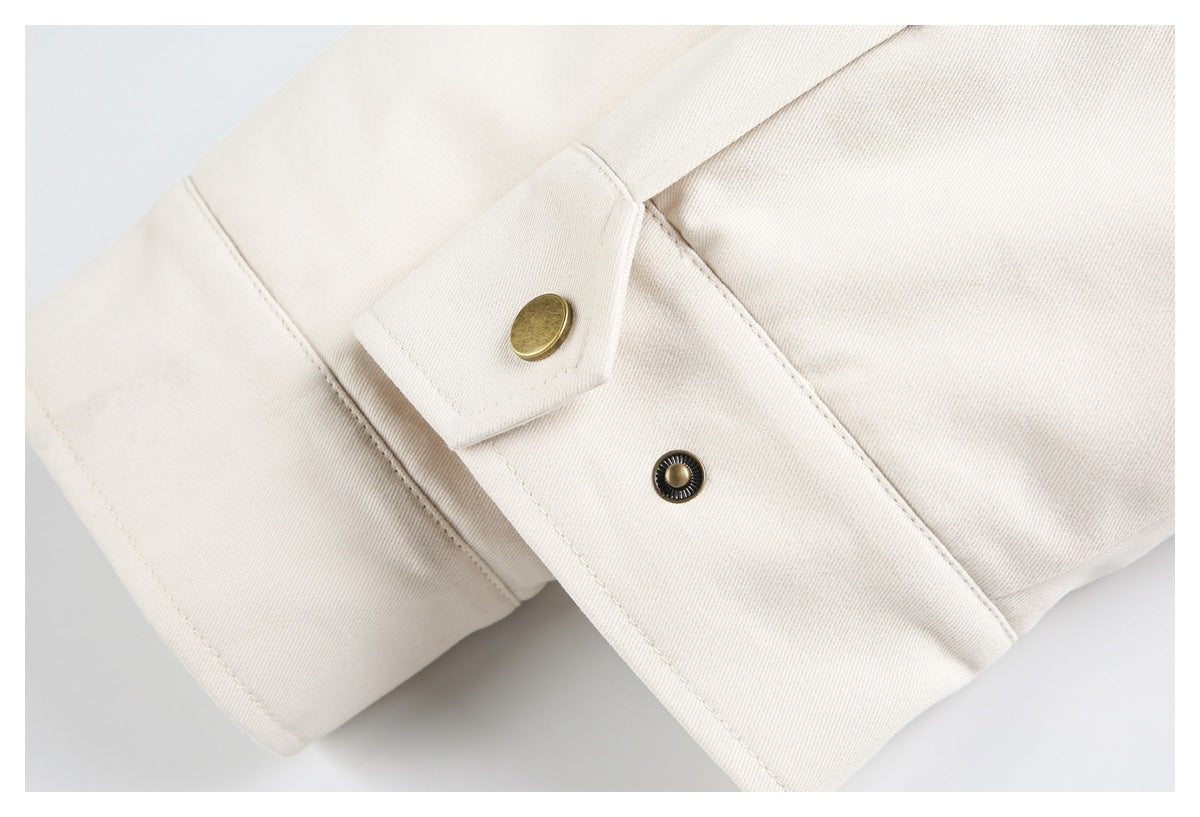 Close-up of an ivory jacket cuff with a brass-colored snap fastener.