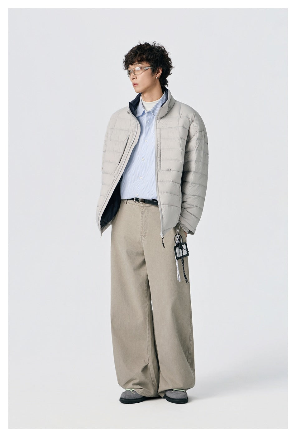 Three-quarter view of a model wearing an open light gray quilted jacket over a blue striped shirt.