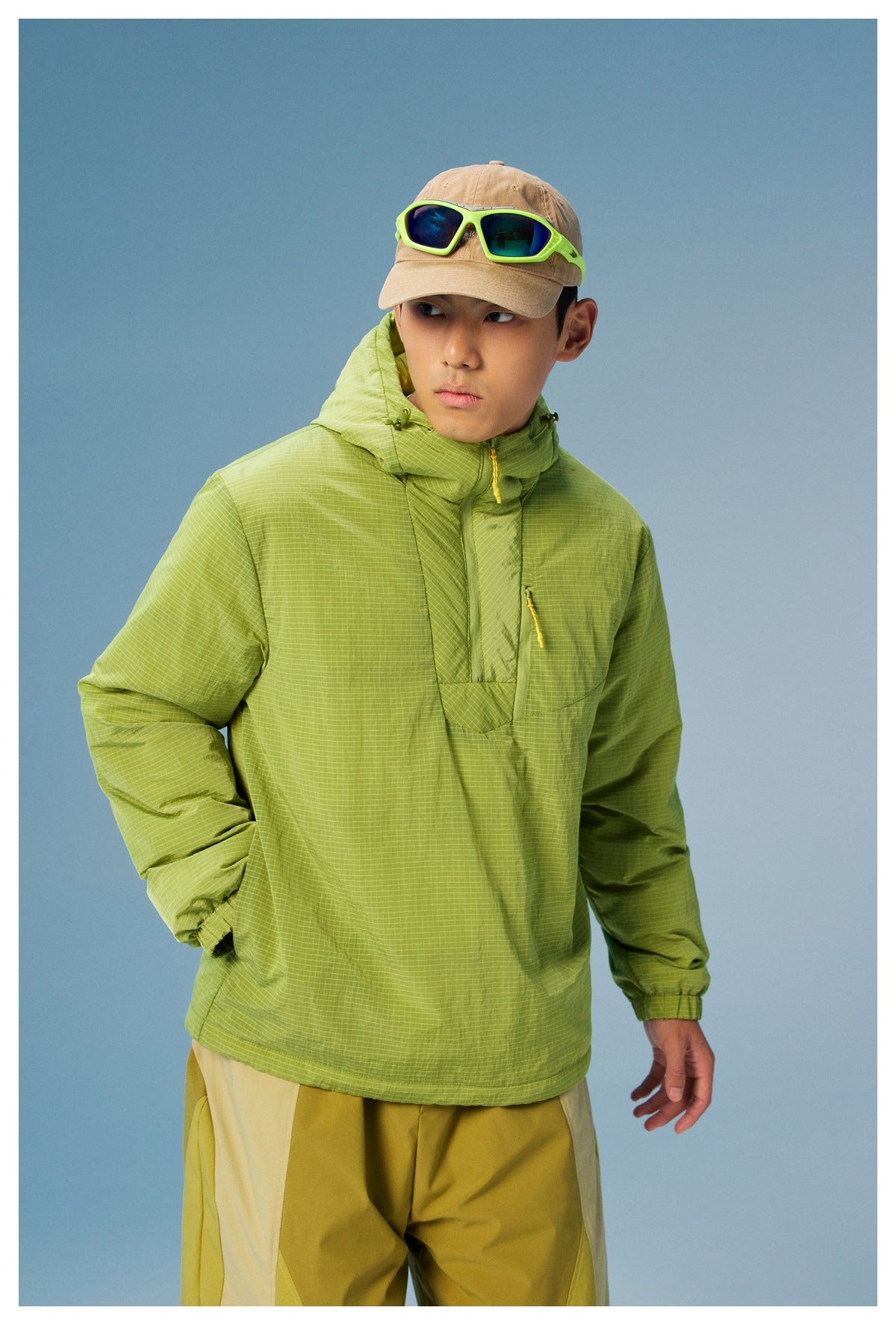 Close-up of a model wearing a lime green grid-pattern hooded pullover with a yellow chest zipper.