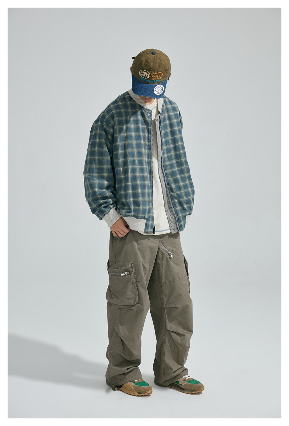 Model wearing the bomber jacket with its blue-and-tan plaid side facing out, paired with olive cargo pants.