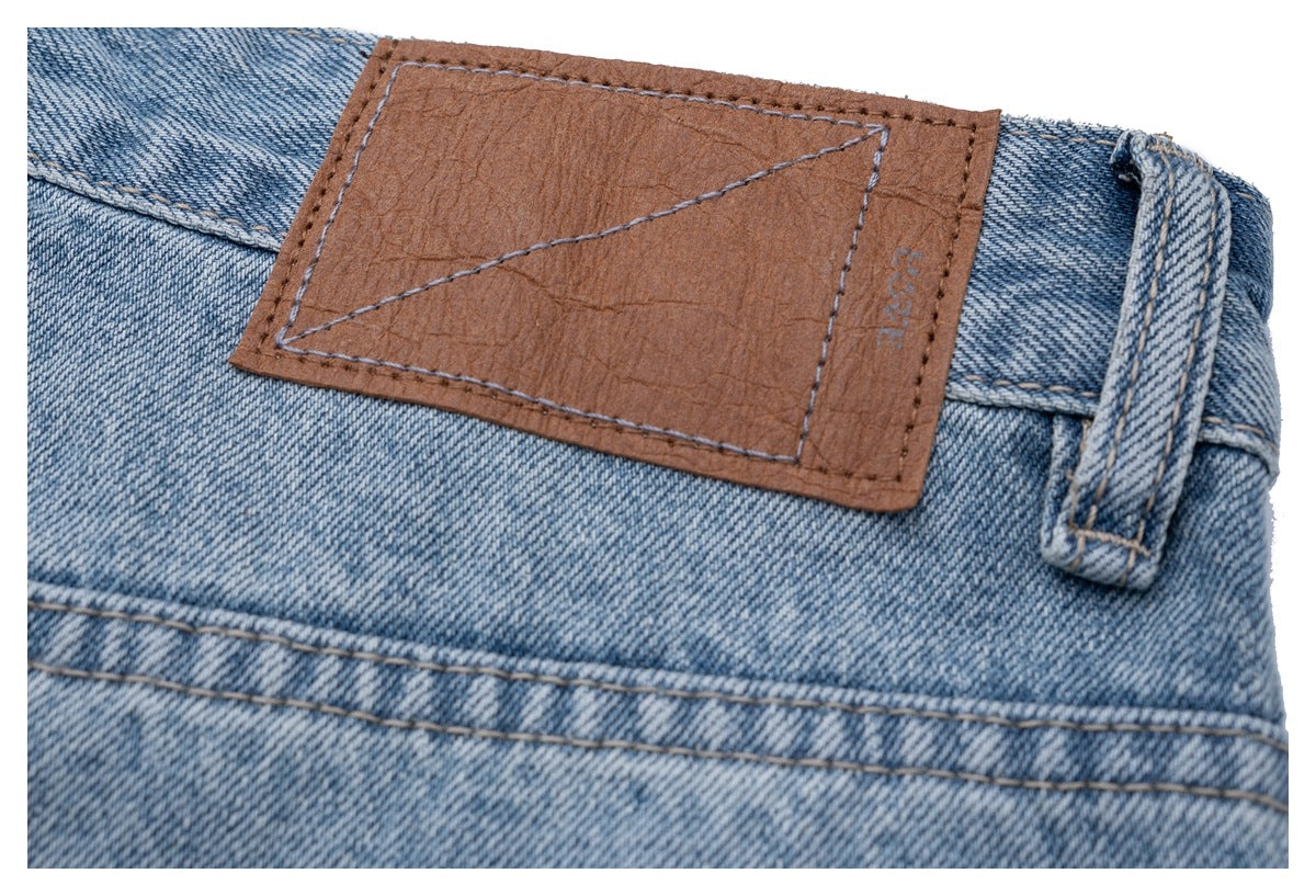 Close-up of a blank brown patch and belt loop on the waistband of light blue jeans.