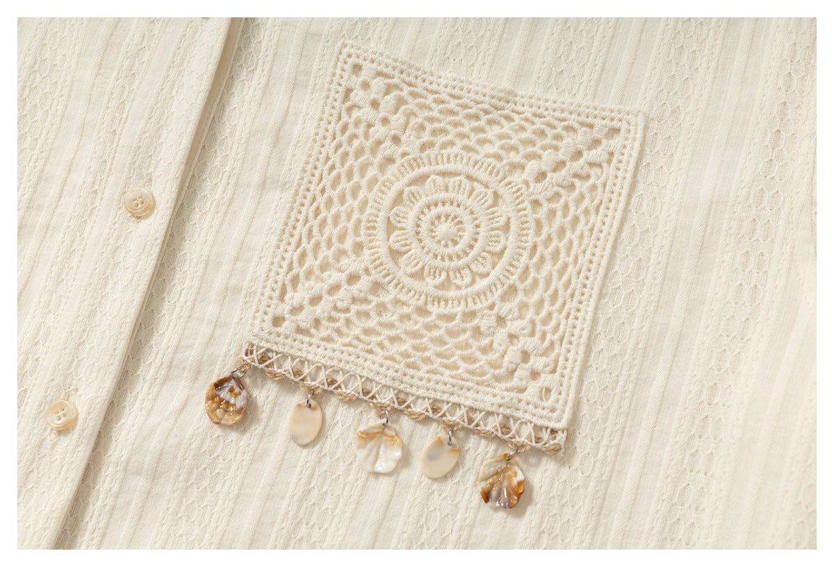 Close-up of an ivory shirt’s crocheted square pocket, decorative shell charms, and button placket.