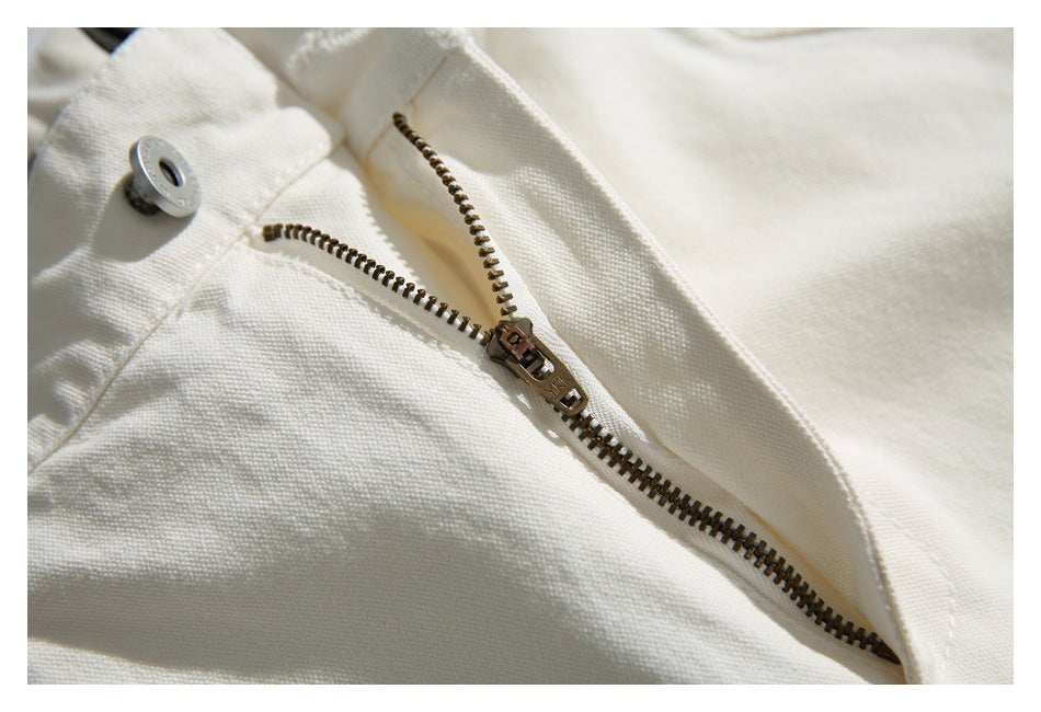 Close-up of off-white trousers showing a metal button and bronze-toned zipper.