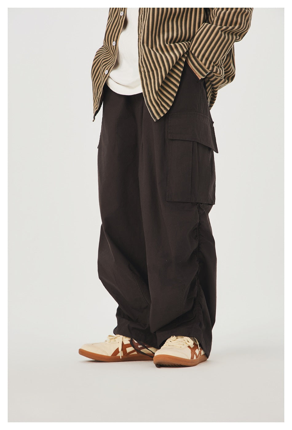 Model wearing dark brown baggy cargo pants with a large flap pocket, shown from the front-side.