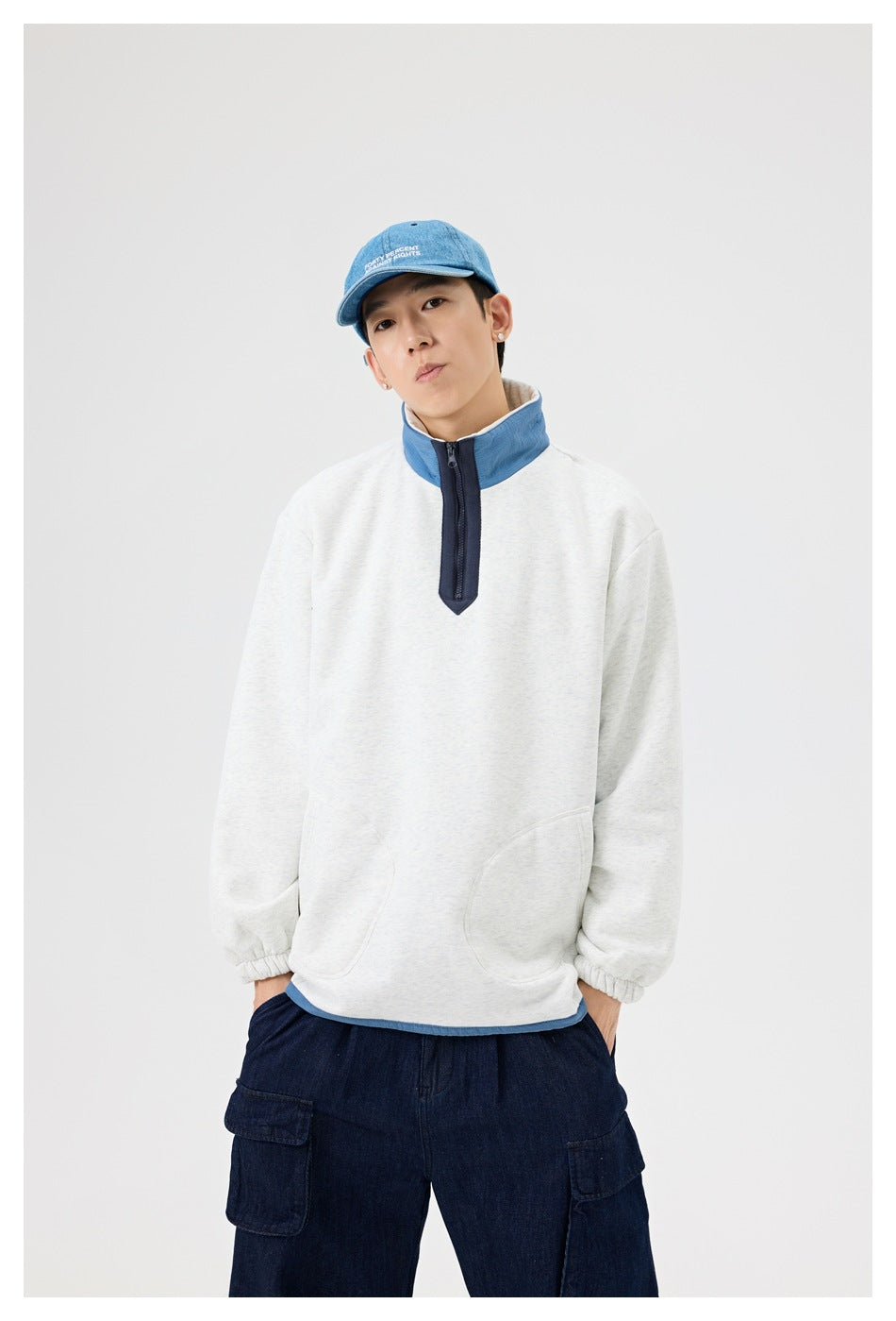 Model wearing a heather gray half-zip sweatshirt with blue stand collar and navy zip placket, front view