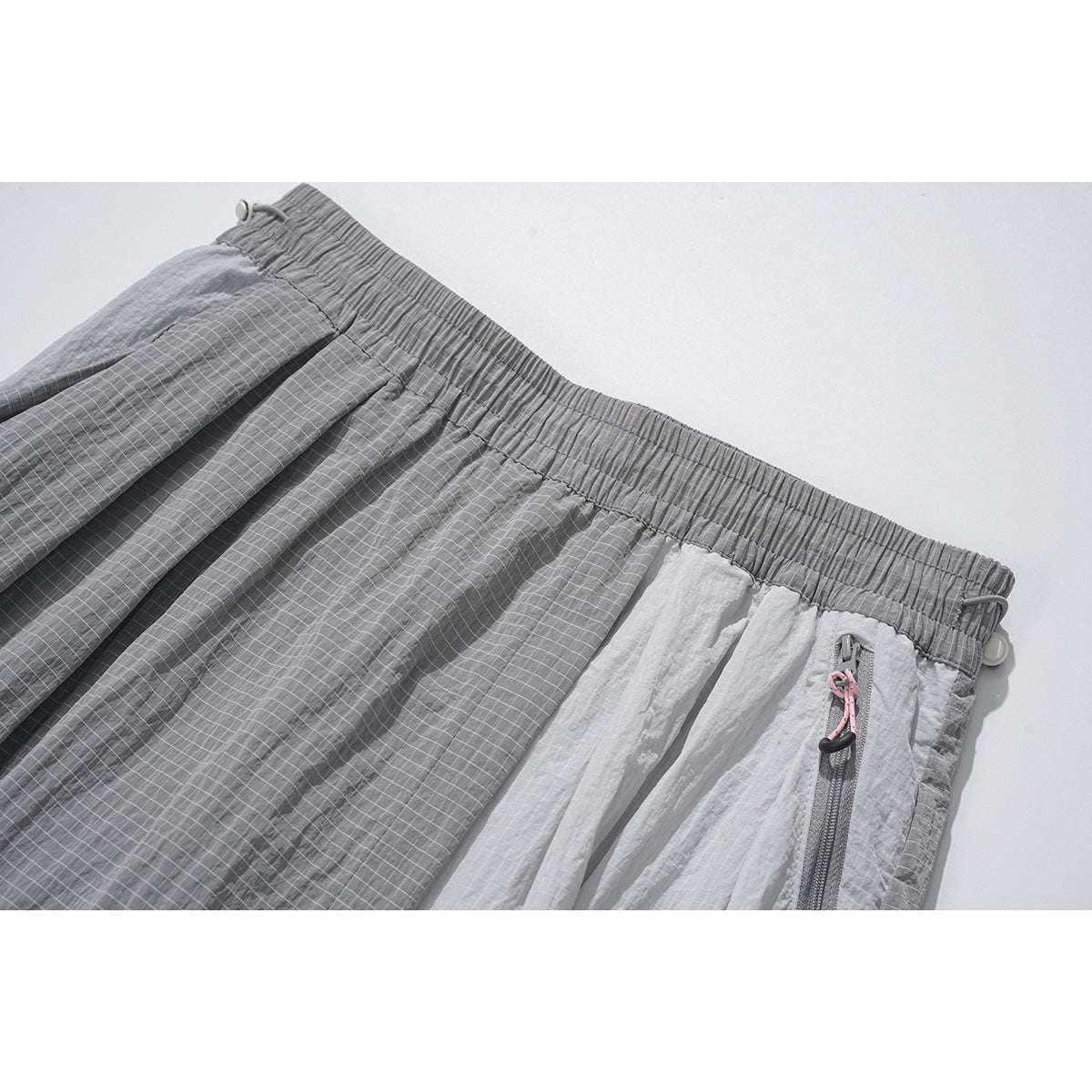 Close-up of gray and white panelled wide-leg bottoms with a fine grid pattern, elastic waistband and zip pocket.
