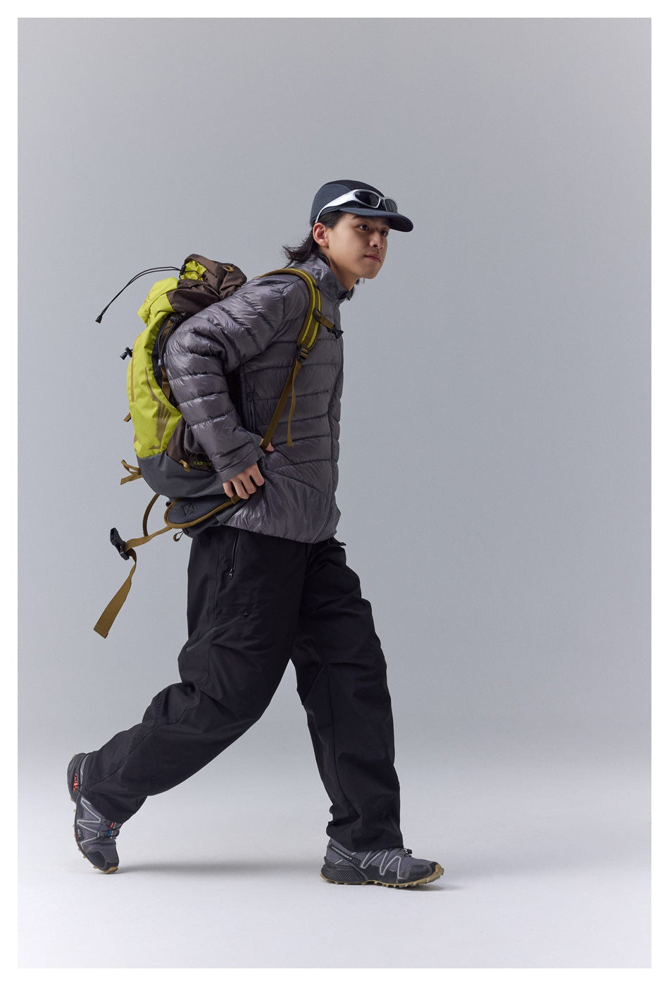 Model wearing a charcoal quilted zip jacket with black outdoor pants and a lime hiking backpack.