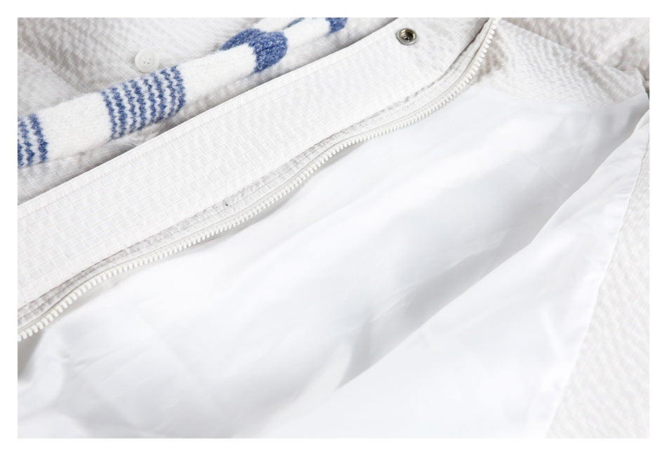 Close-up of a white garment showing its lining, zipper, snap button, and a blue-and-white striped knit detail.