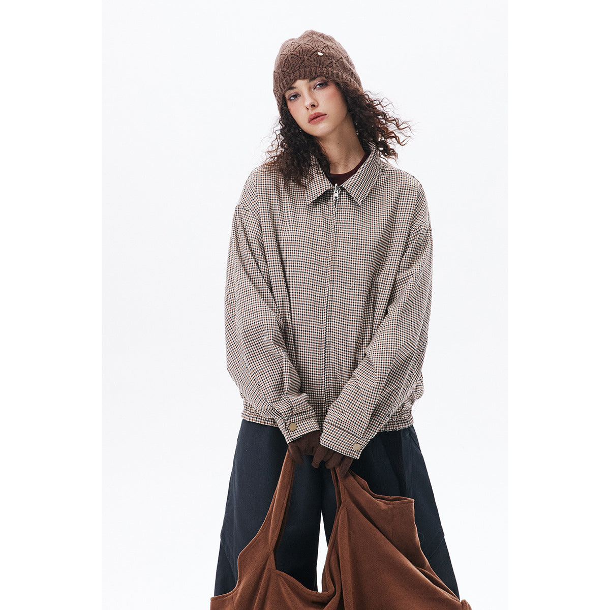 Model wearing a beige-and-brown check zip jacket with a pointed collar, navy wide-leg trousers, and a brown knit beanie.