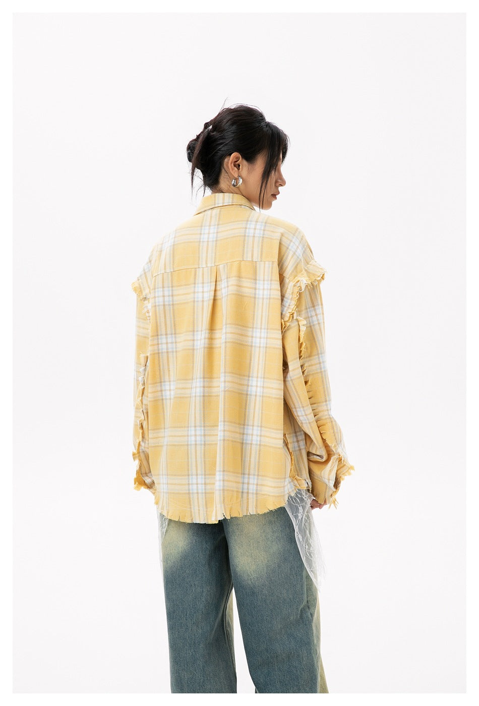 Back view of a model in an oversized yellow plaid shirt with frayed edges and lace below, with faded jeans