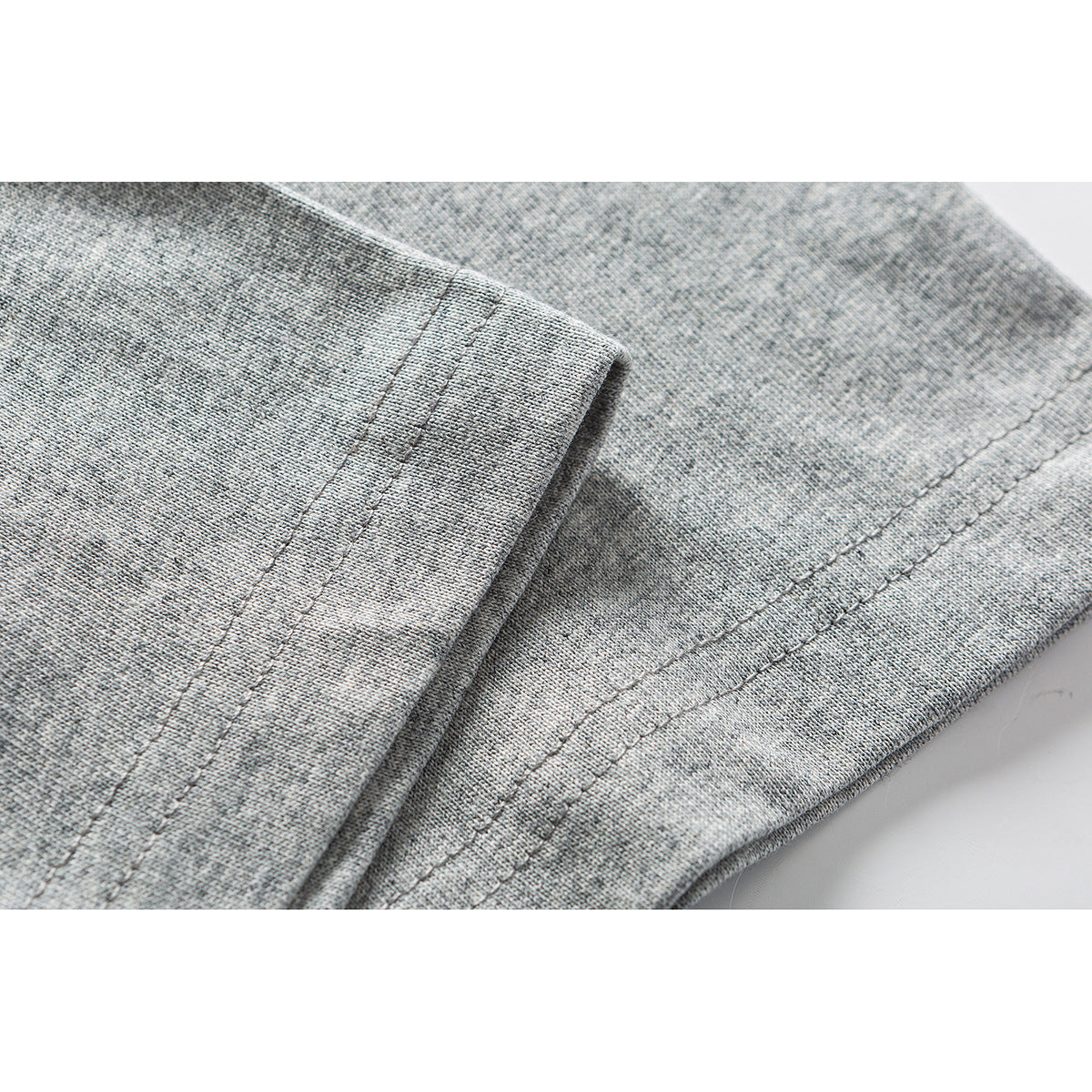 Close-up of heather gray T-shirt fabric showing stitched hems and a folded sleeve edge.