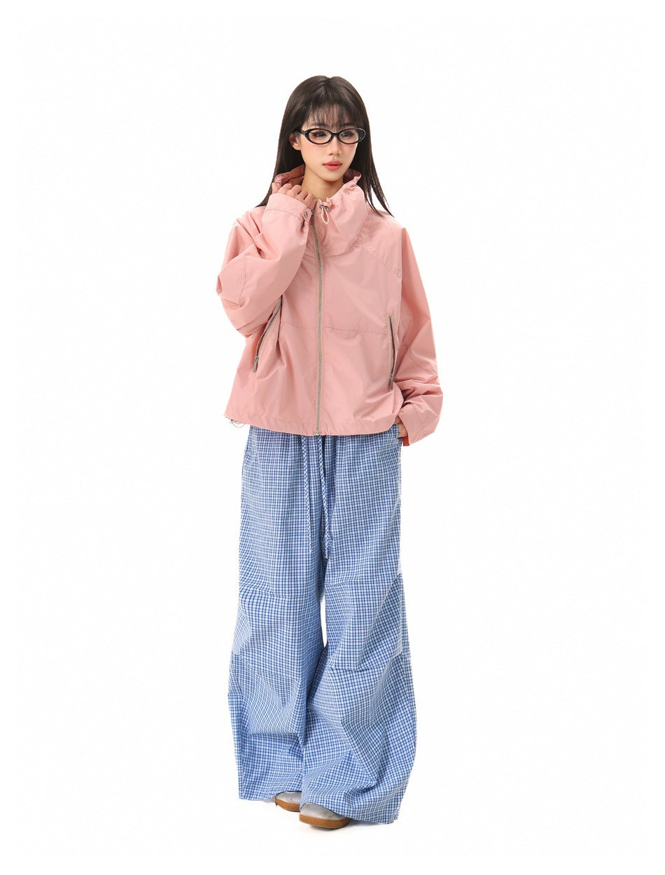 A model wears a light pink high-collar zip jacket with blue checked wide-leg trousers.