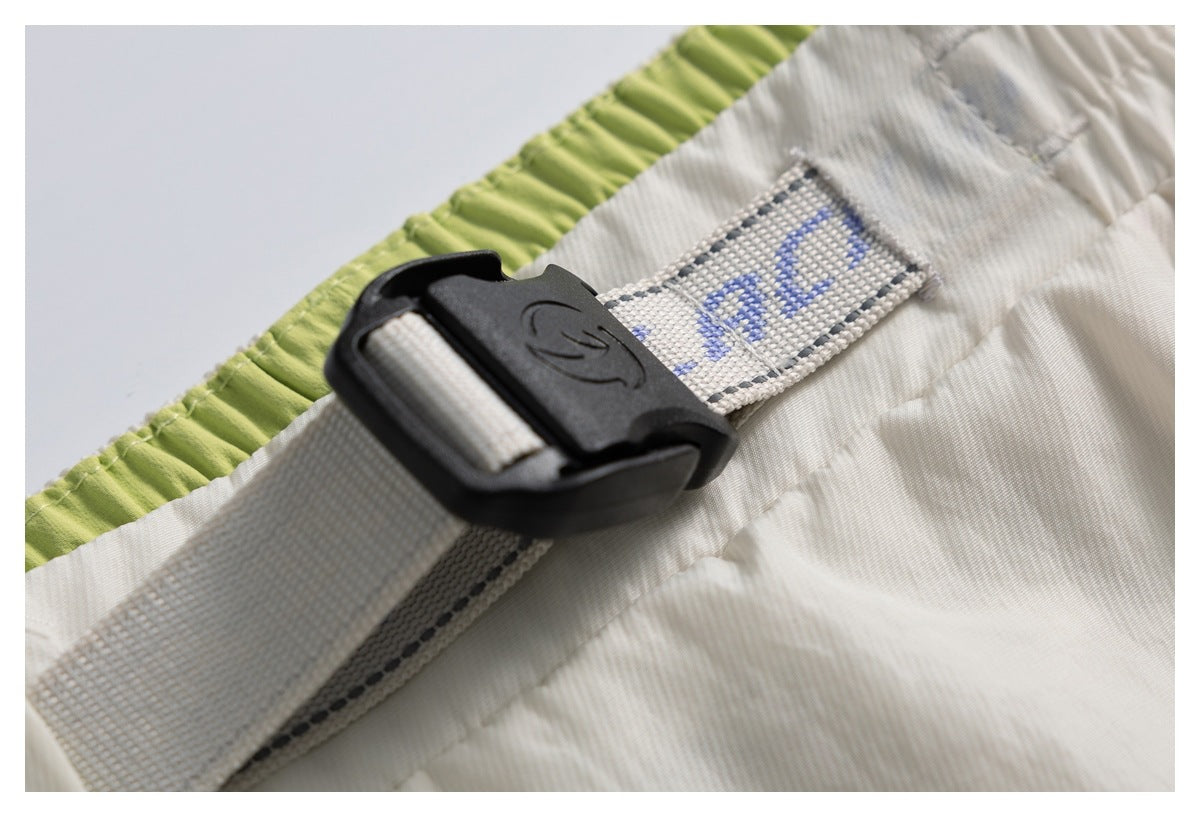 Close-up of a black plastic buckle on a gray woven strap attached to cream fabric, with a lime-green gathered edge.