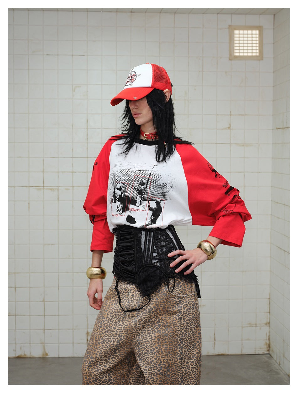 Model wearing a white graphic raglan shirt with red sleeves, a black corset belt, and loose tan leopard-print pants.