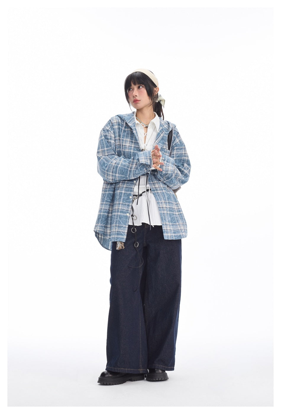 Front view of a model wearing a blue-and-white plaid hooded shirt jacket over a white blouse and wide dark jeans.