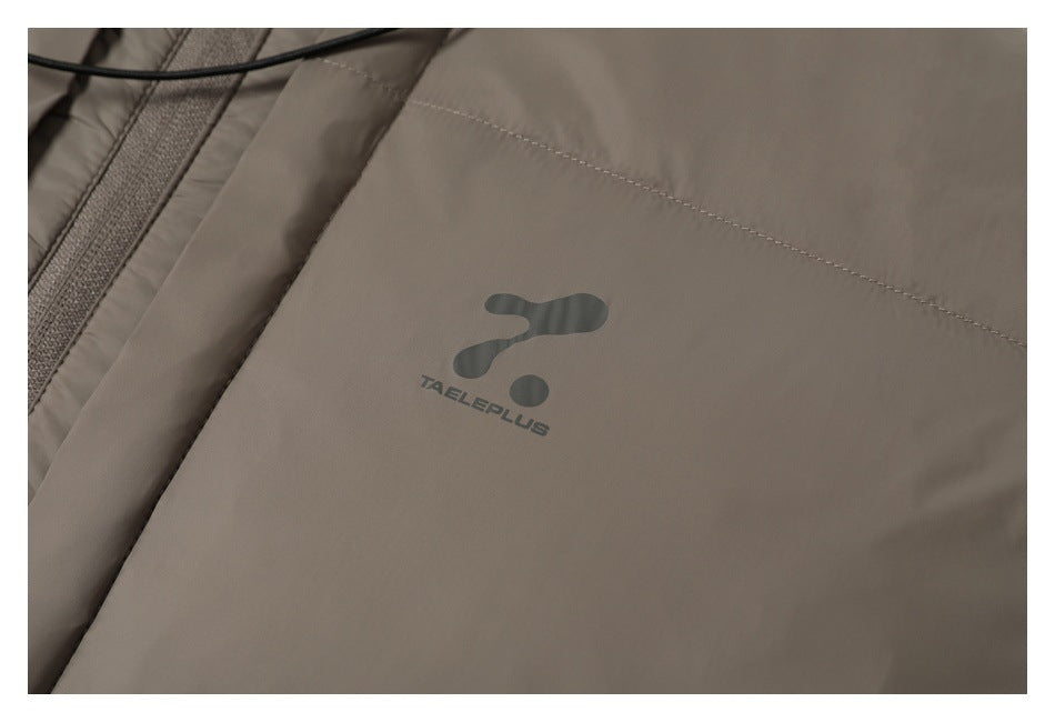 Close-up of a small dark TAELPLUS logo printed on the taupe jacket.