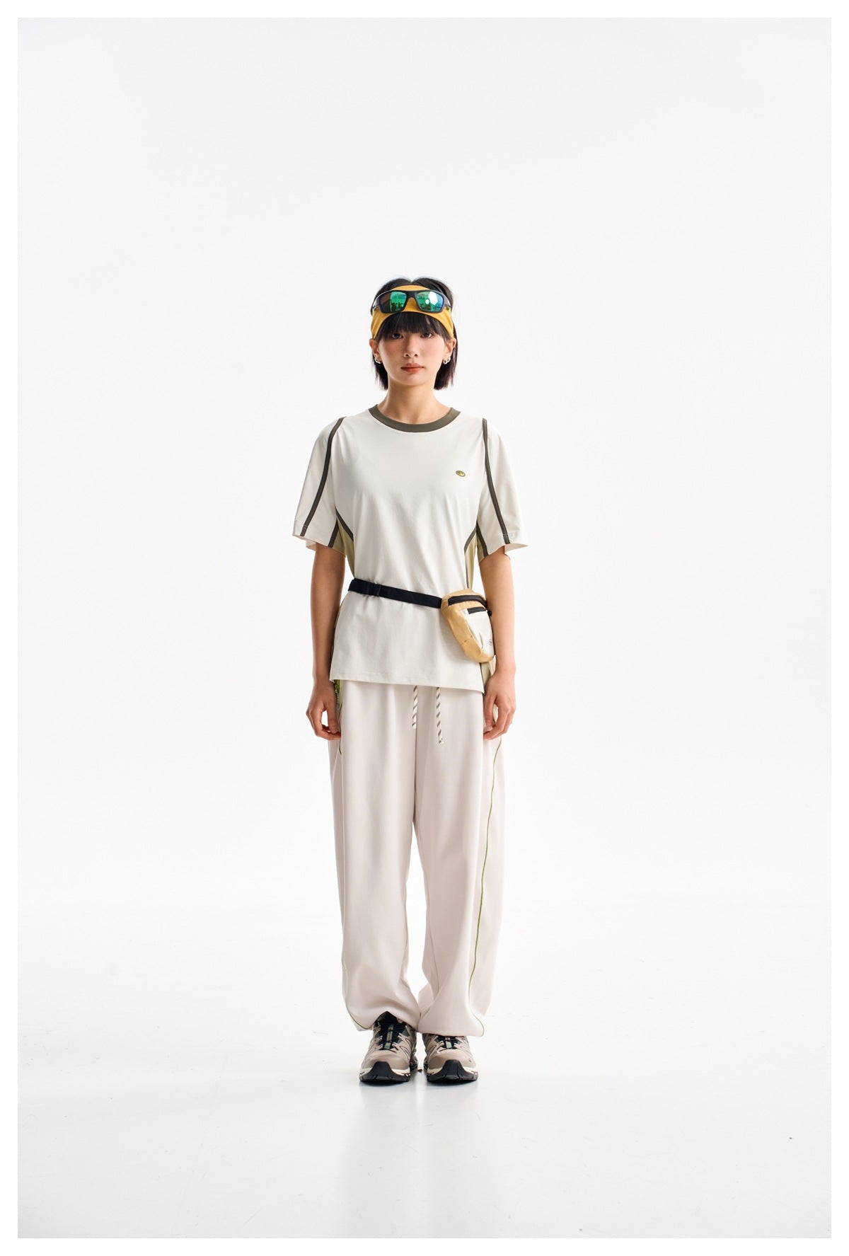 Model wearing a white short-sleeve shirt with olive and dark trim, loose light pants, and a waist pouch.