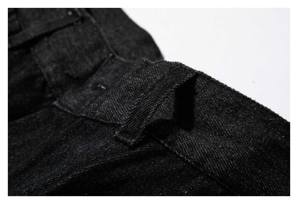 Close-up of black textured fabric with overlapping stitched seams and a folded garment edge.