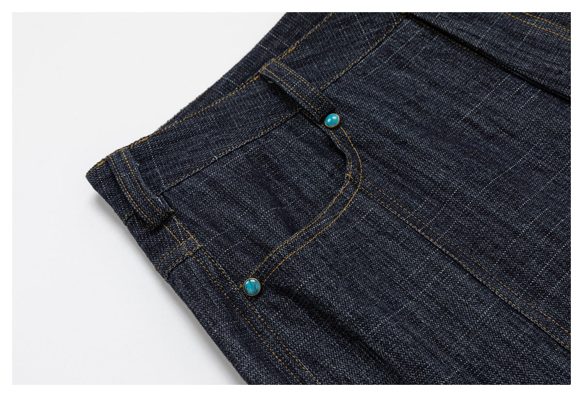 Close-up of a front pocket on dark indigo pants, with contrast stitching and turquoise-colored rivets.