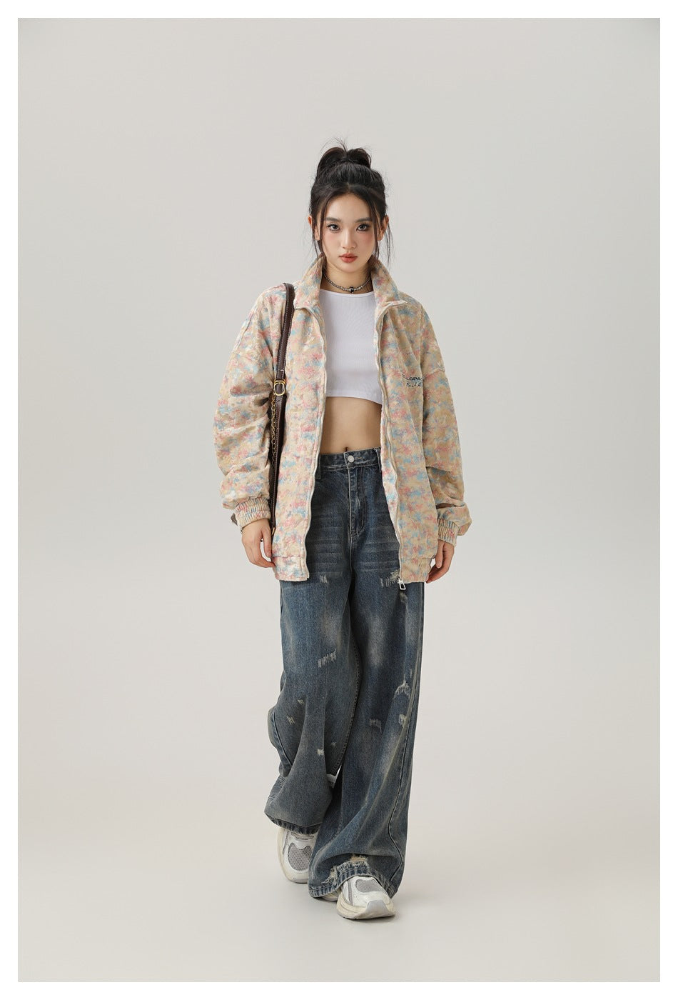 Full-length view of a model wearing a pastel multicolor zip-up jacket and loose, distressed jeans.