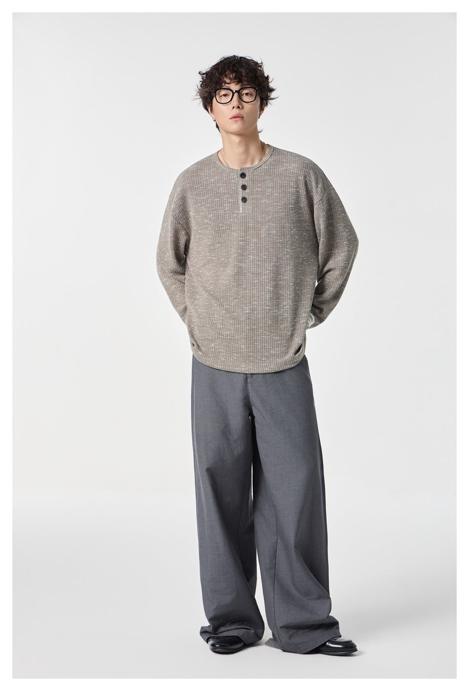 Full-length model wearing a taupe-gray Henley with a three-button placket and gray wide-leg trousers.