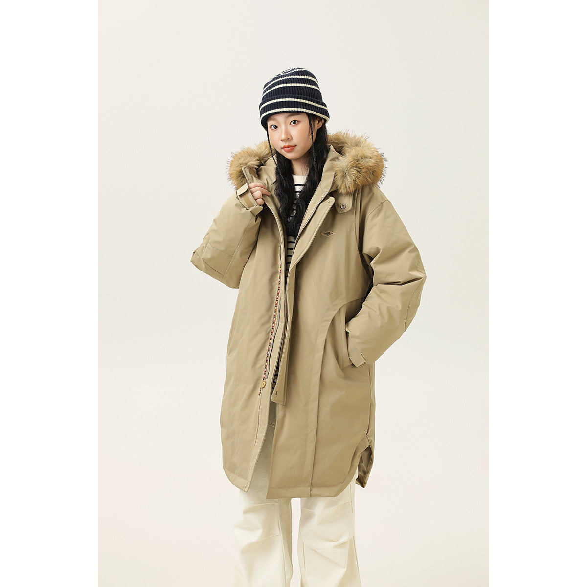Model wearing a long beige parka with a tan fur-trimmed hood, shown from the front.