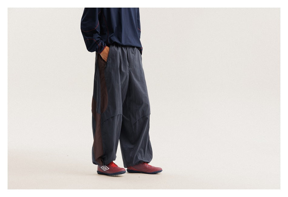 Side view of a model wearing loose charcoal pants with a brown side panel and gathered hems.