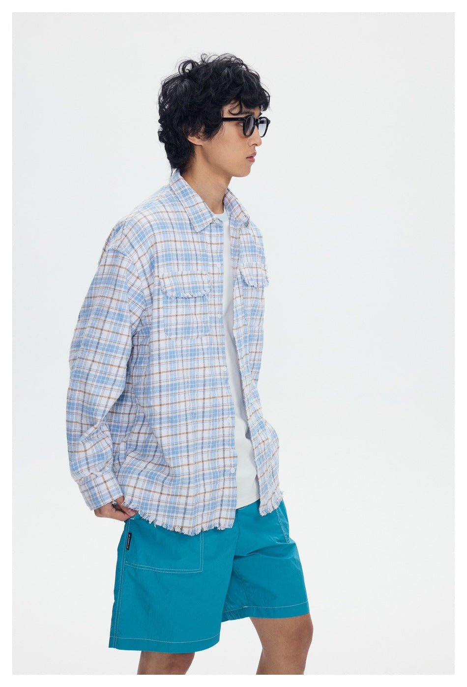 Side view of a model wearing an open light blue plaid shirt with frayed edges and turquoise shorts.