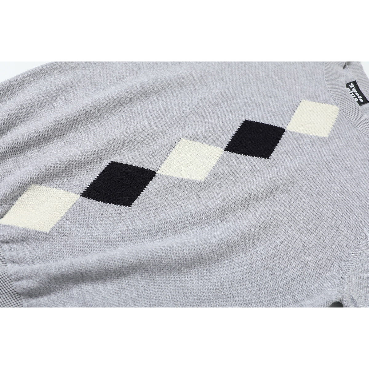 Close-up of a light gray knit sweater with a diagonal row of cream and black diamond shapes.