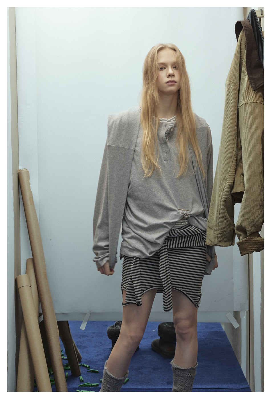 Model wearing an oversized gray top over a black-and-gray striped skirt, with a gray layer draped over her shoulders.