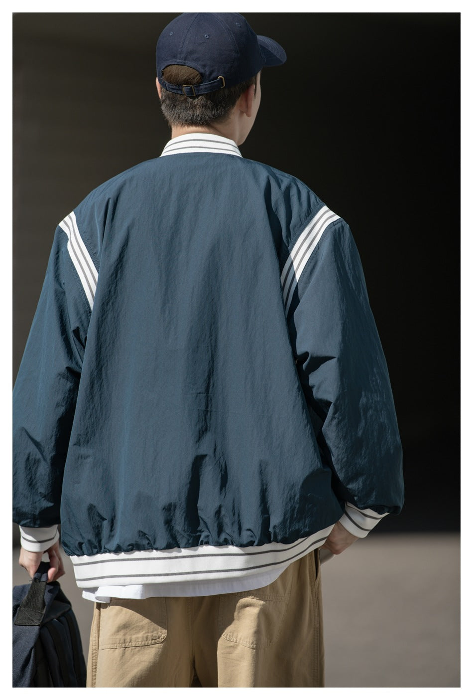 Rear view of a model wearing a dark teal jacket with white striped shoulder panels, collar, cuffs and hem.