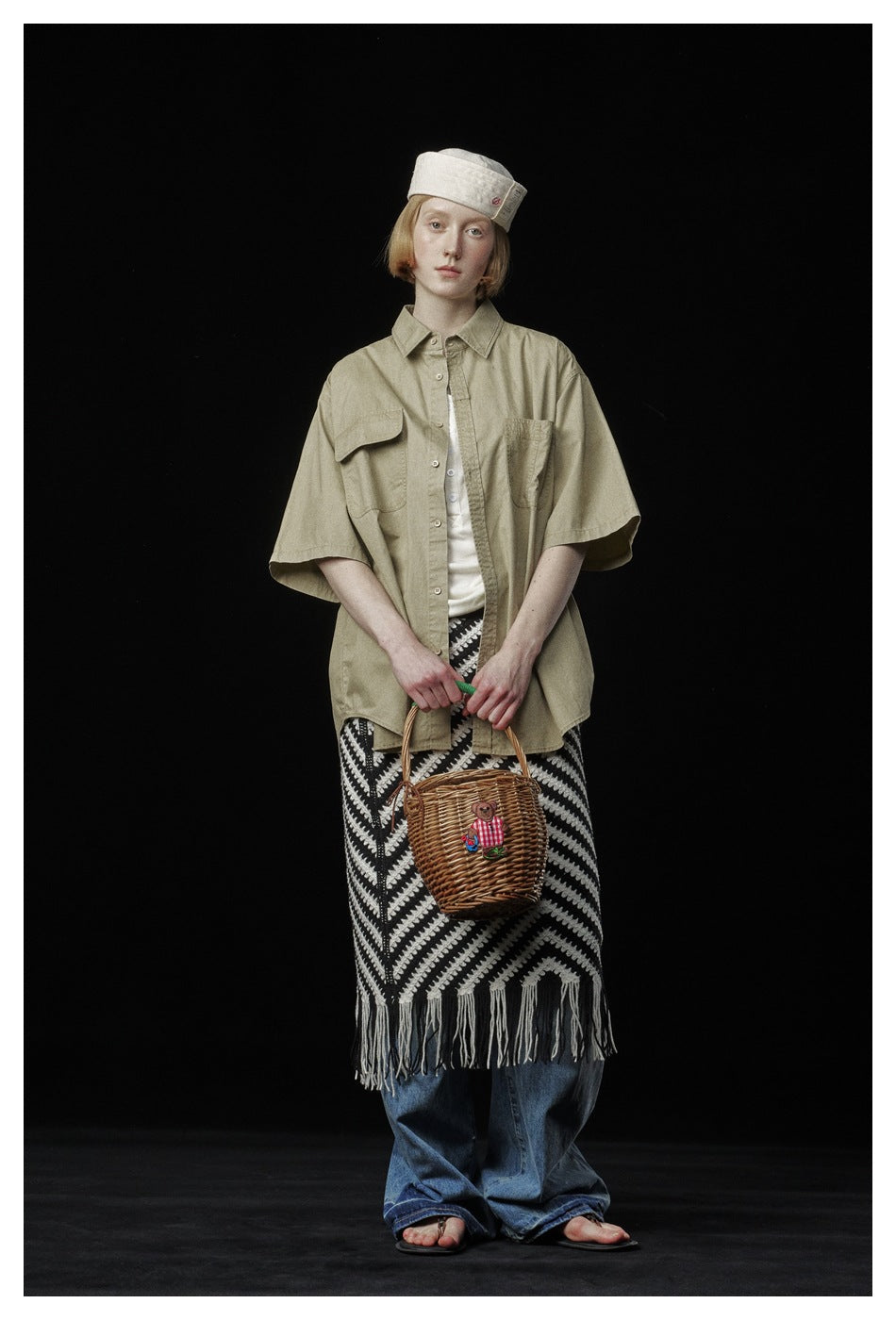 Model wearing a khaki short-sleeve work shirt open over a white top with a striped skirt, jeans and basket