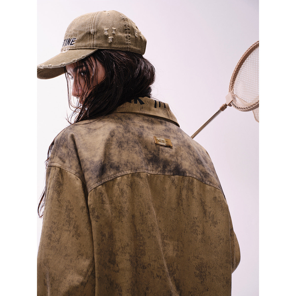 Close-up of the mottled tan-brown jacket's back yoke and small patch, with the model wearing a distressed cap.