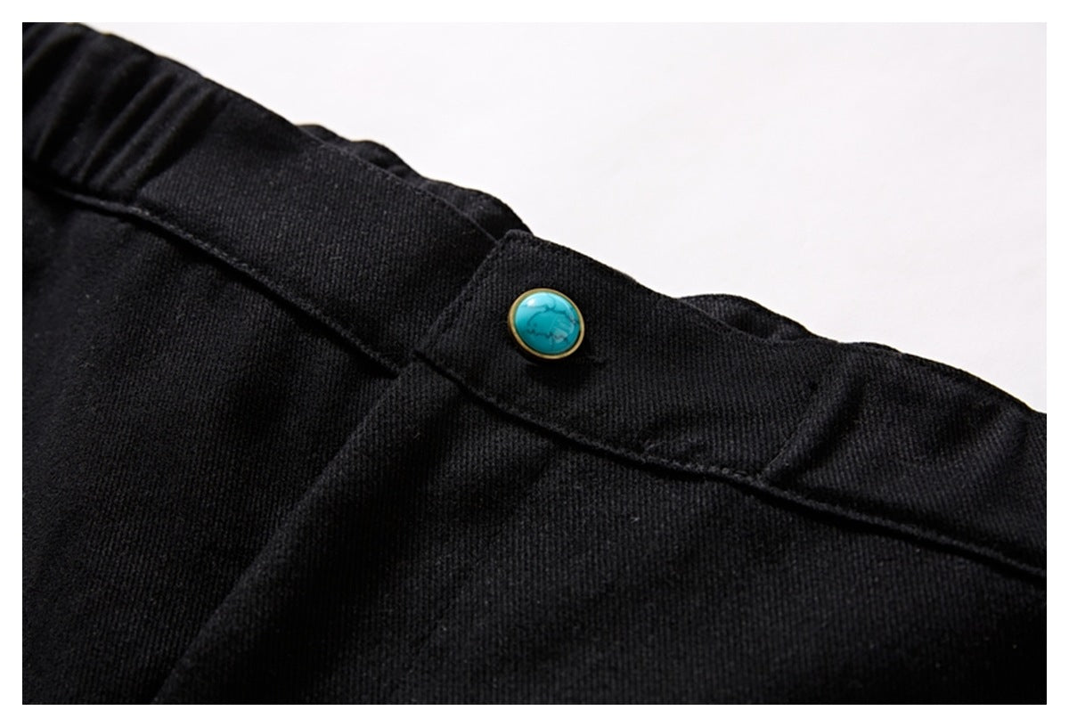 Close-up of a turquoise button on the waistband of black shorts, with stitching and textured fabric visible.