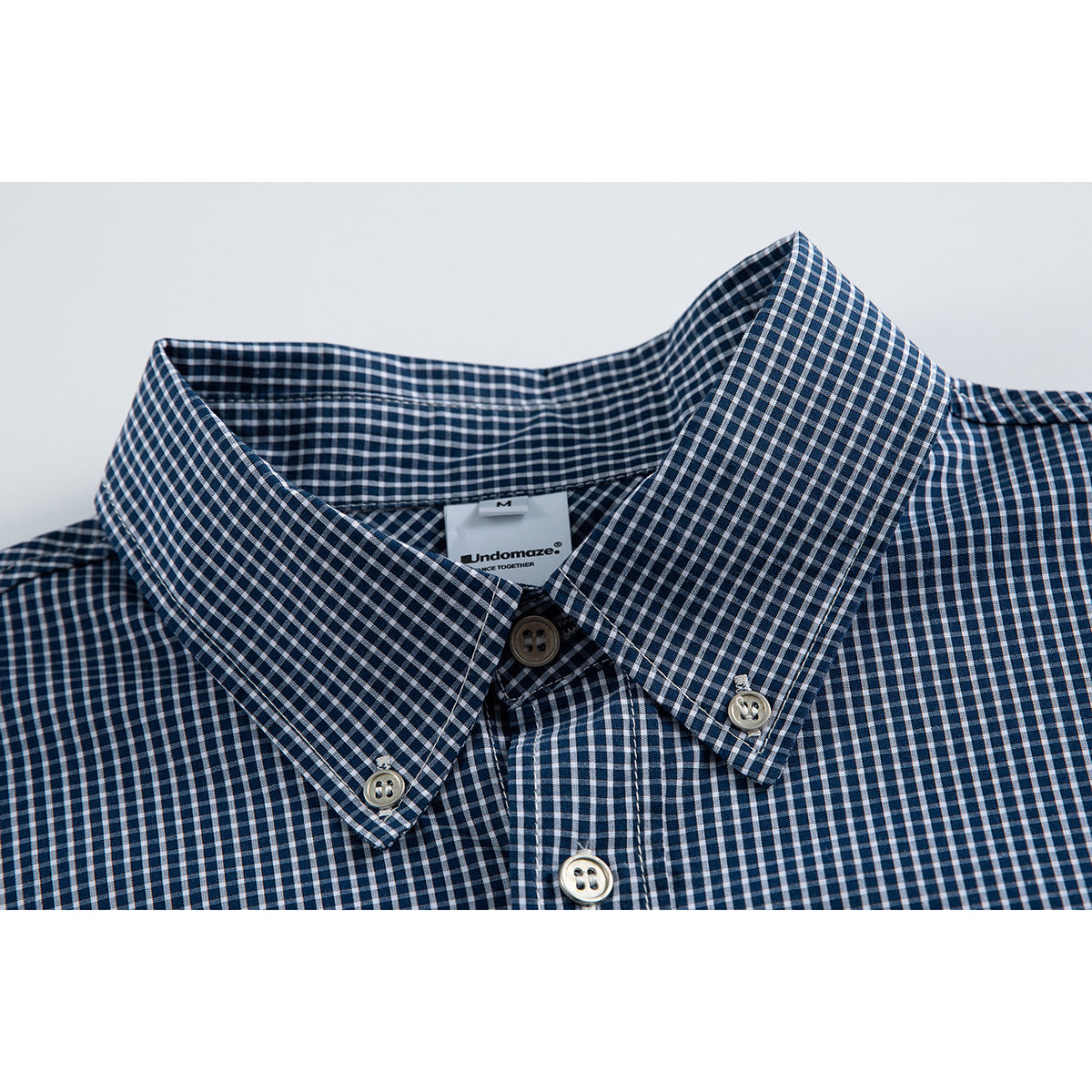 Close-up of a navy-and-white gingham shirt collar with button-down points and front buttons.
